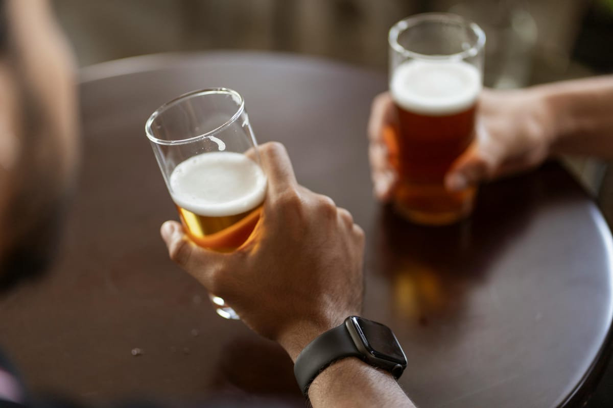 A pint of beer on a wooden table beside a fitness watch.