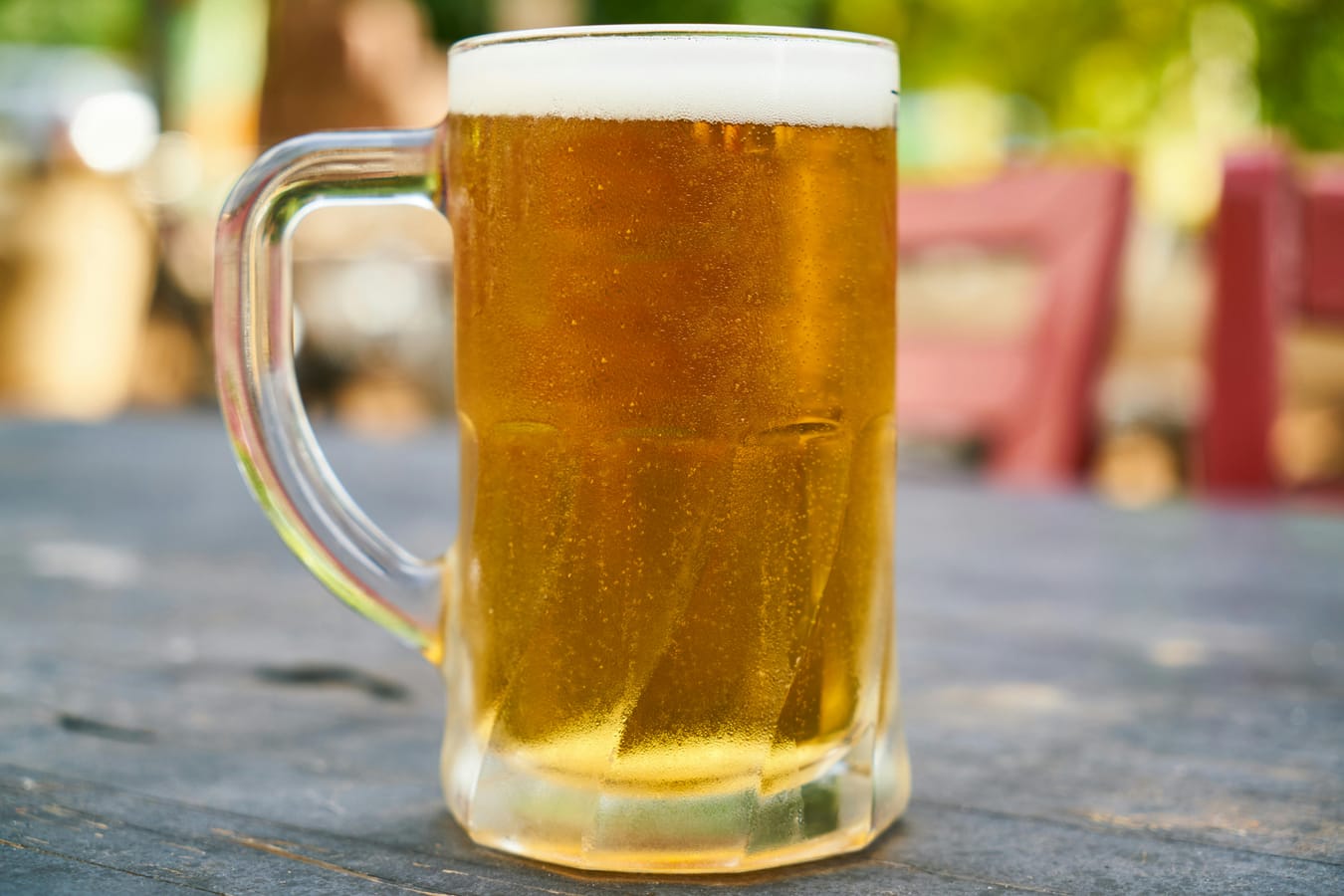 A pint of light beer on an outdoor wooden table beside a pair of running shoes.
