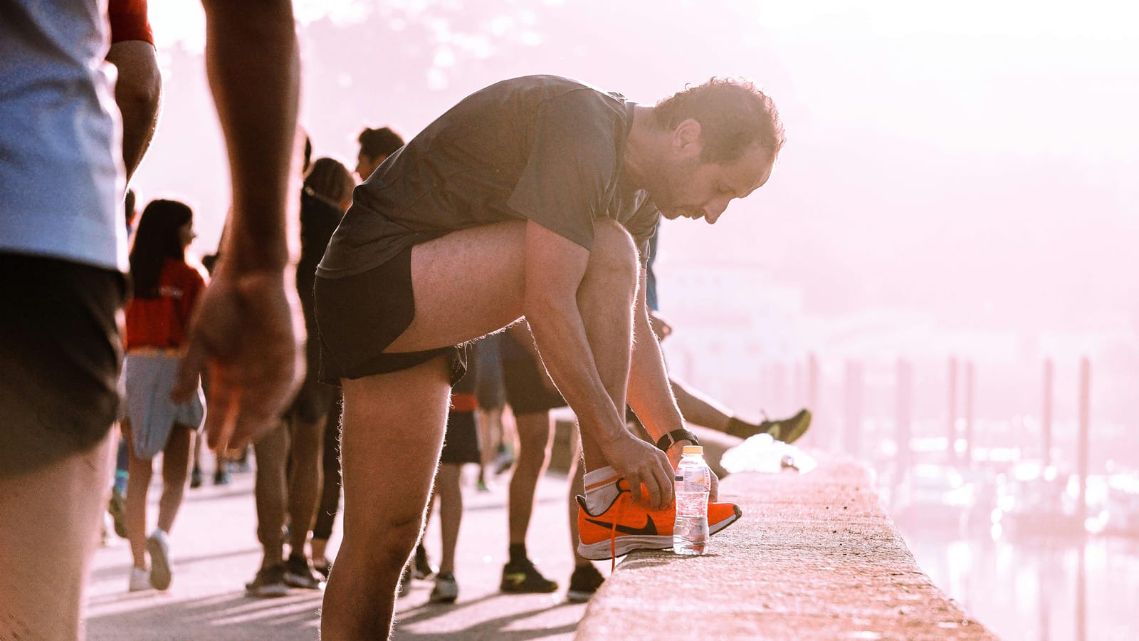 A pair of running shoes and a water bottle on a wooden floor in soft morning light.