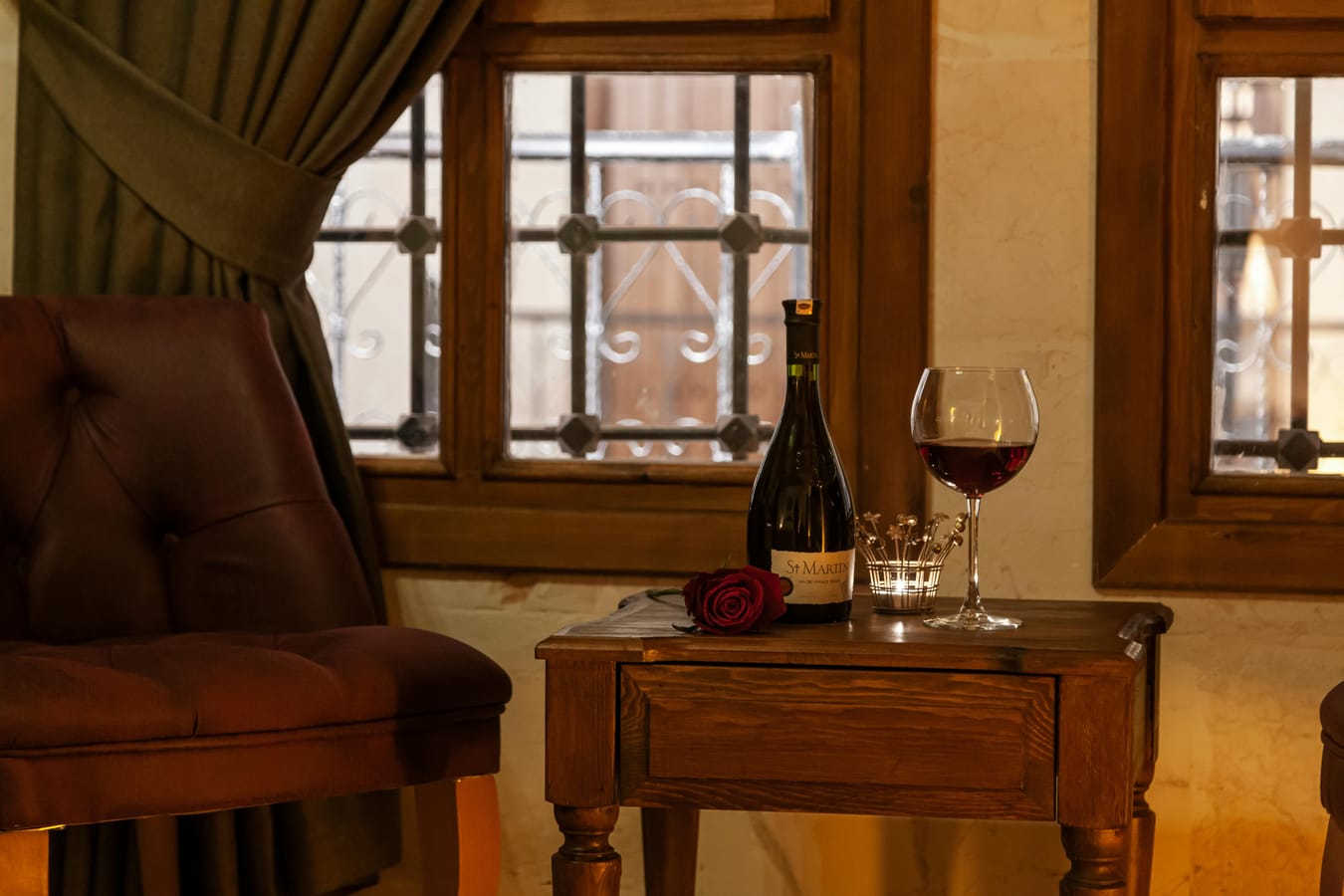 A glass of wine on a wooden side table next to a soft armchair, suggesting evening relaxation.