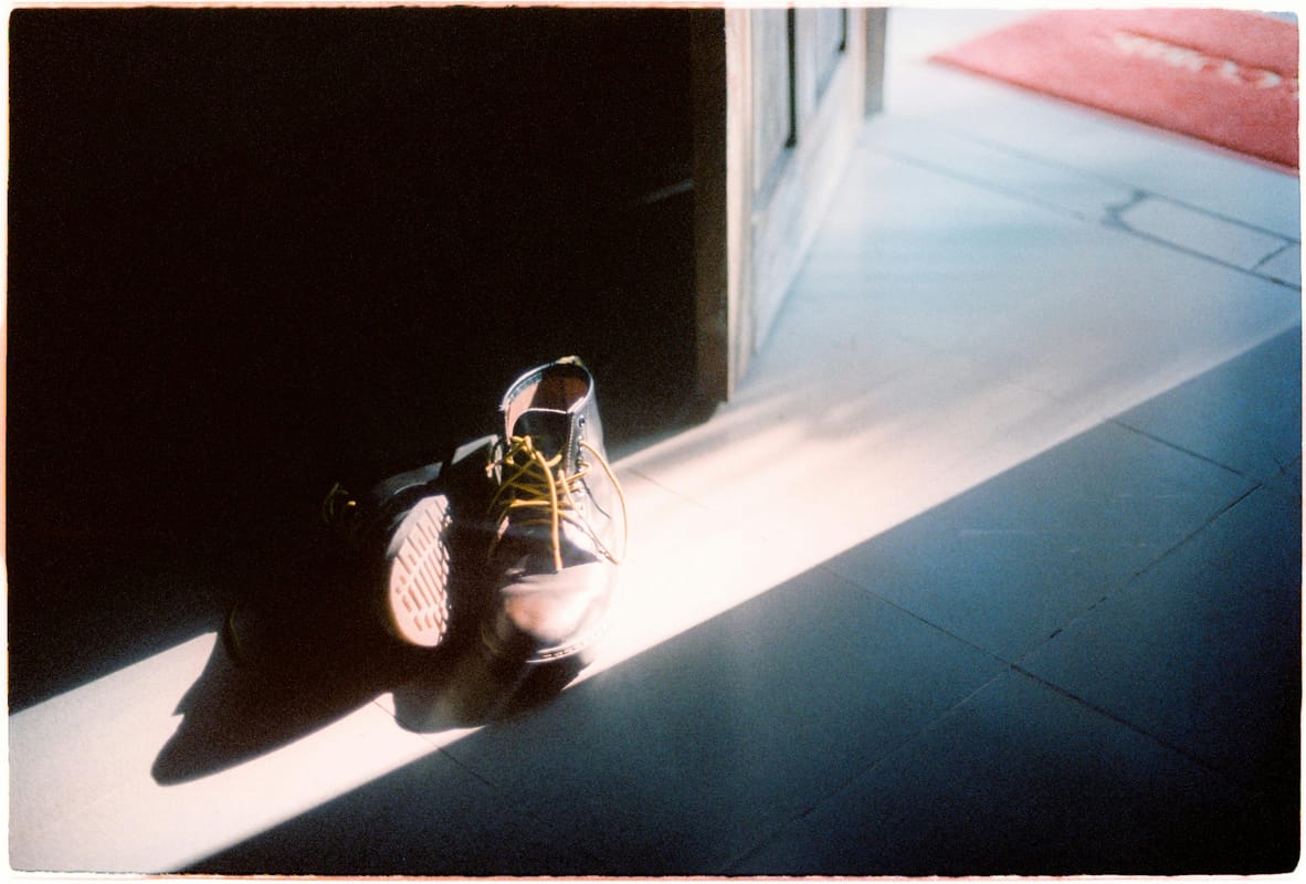 A pair of walking shoes by a doorway in morning light.