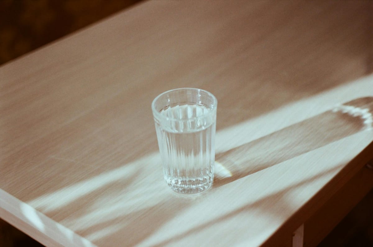 A glass of clear liquid on a wooden table with light passing through.