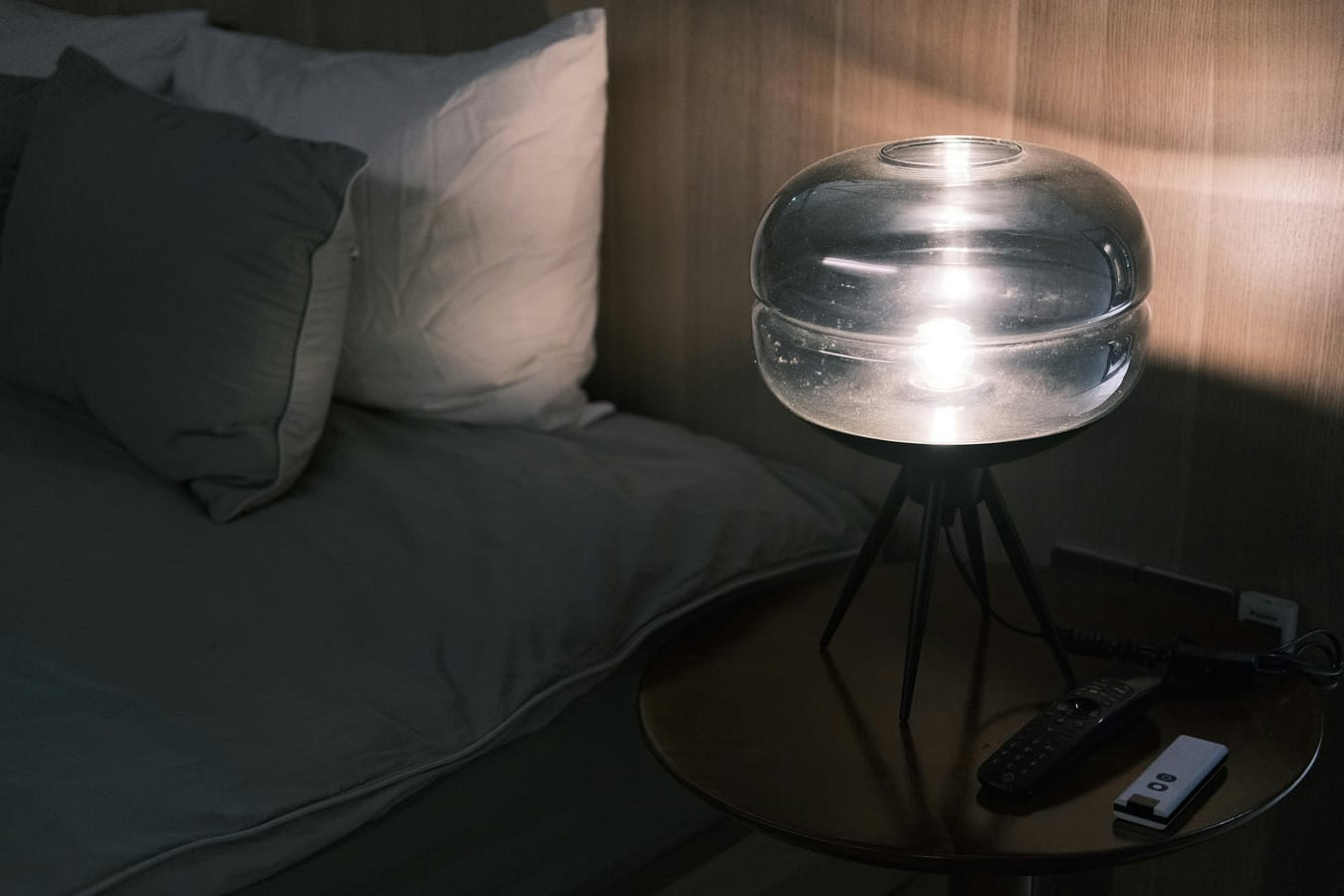 A glass of whisky on a bedside table beside a lit lamp in evening light.