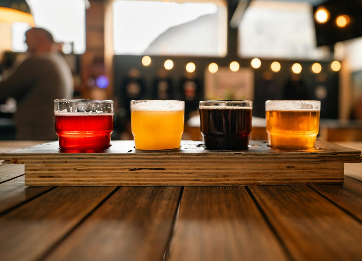 Three pint glasses of different beers (light lager, IPA, stout) arranged on a wooden bar.