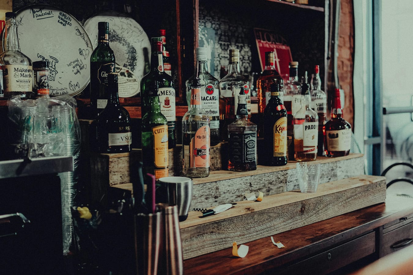 A row of spirit bottles on a wooden bar with a single shot glass in the foreground.