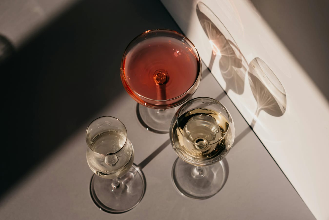 Three wine glasses showing red, white, and rosé arranged on a wooden table in soft natural light.