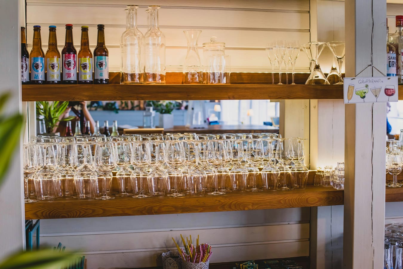 A pint of beer, a glass of wine, and a cocktail glass arranged on a wooden bar in soft light.