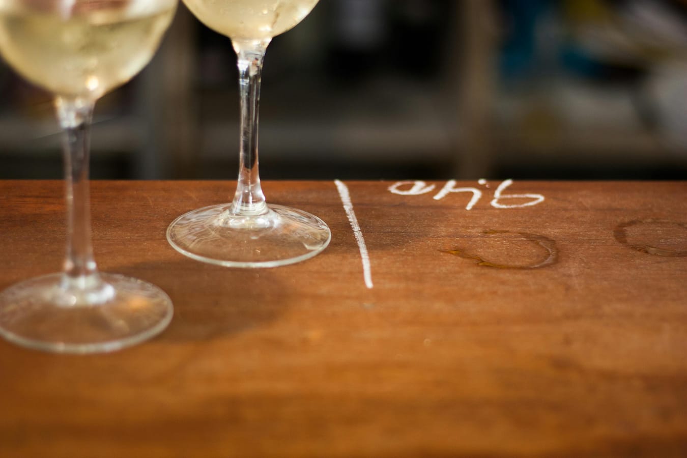 A glass of dry white wine and a tape measure on a wooden table in soft natural light.