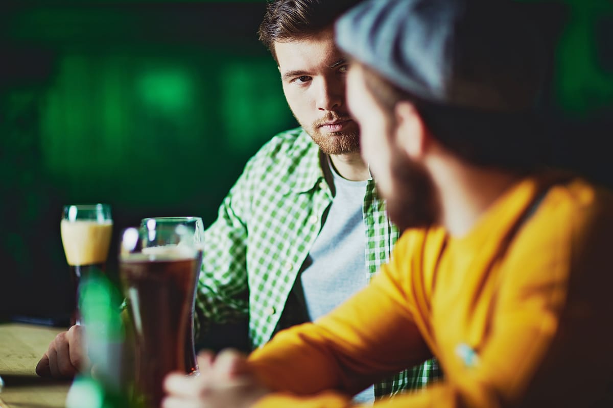 Freunde unterhalten sich an einem Kneipentisch mit Gläsern vor sich.
