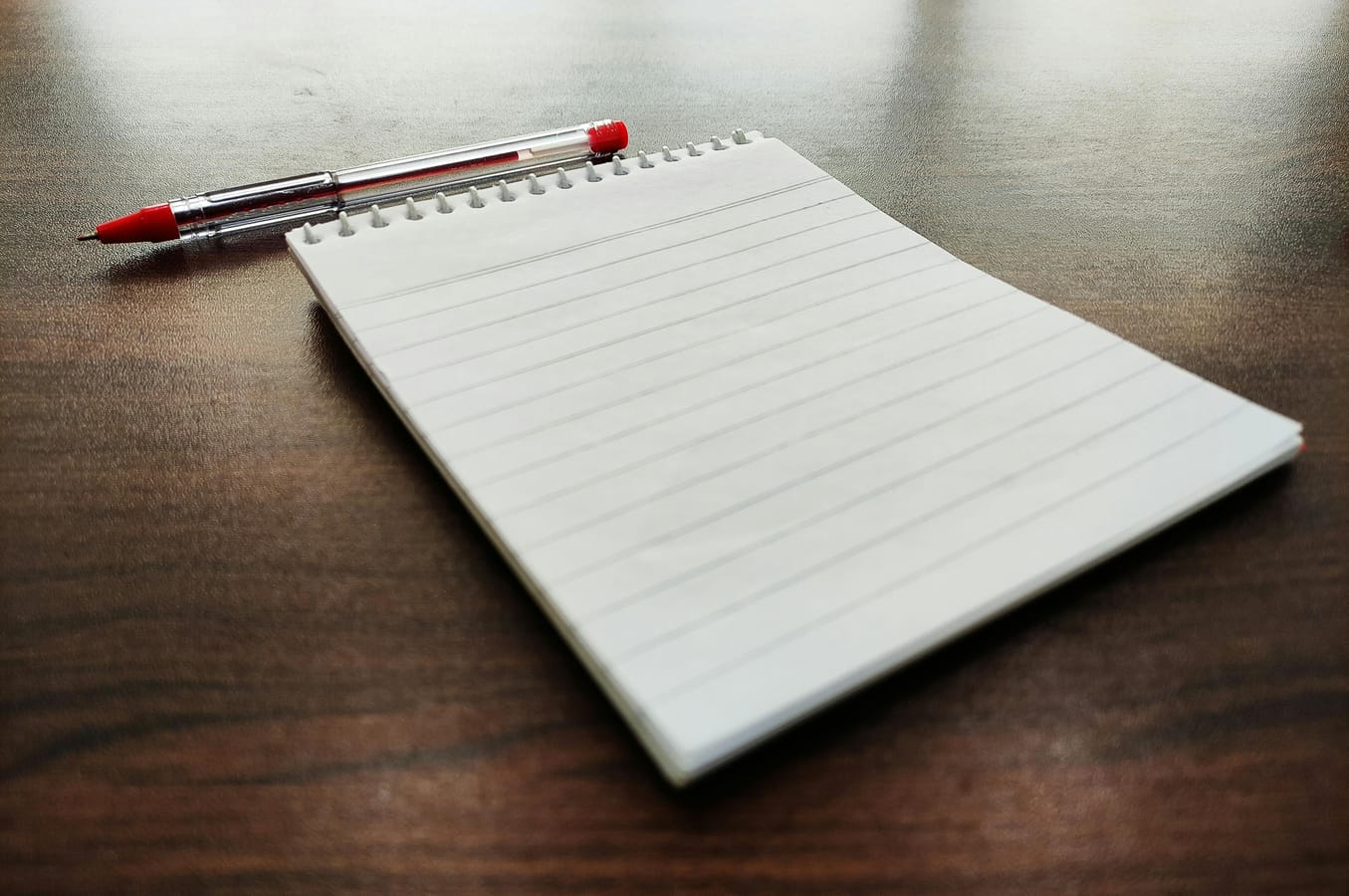 A simple wooden table with a small notebook, a pen, and a glass of beer.