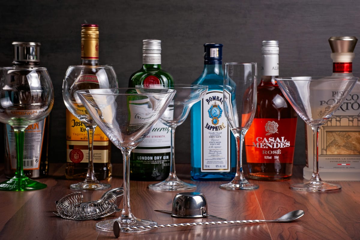 Different drink glasses side by side on a wooden bar.
