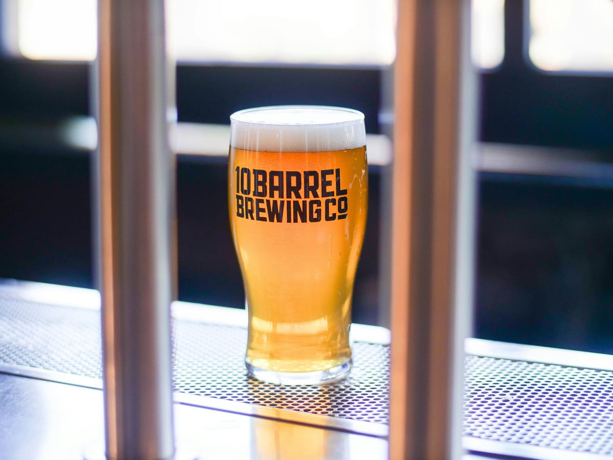 A full pint glass of golden beer on a wooden bar with soft warm lighting.
