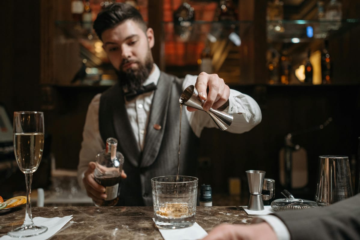 A pint, a wine glass, and a spirit measure side by side on a wooden bar.