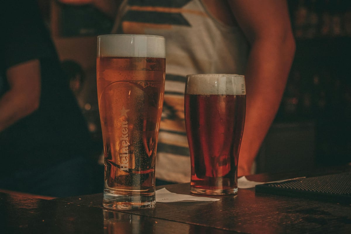 A glass of water beside a pint of beer on a wooden bar.