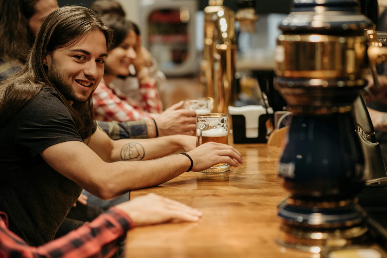 Several pints of beer on a wooden bar with a clock visible in the background suggesting the time element of binge drinking.