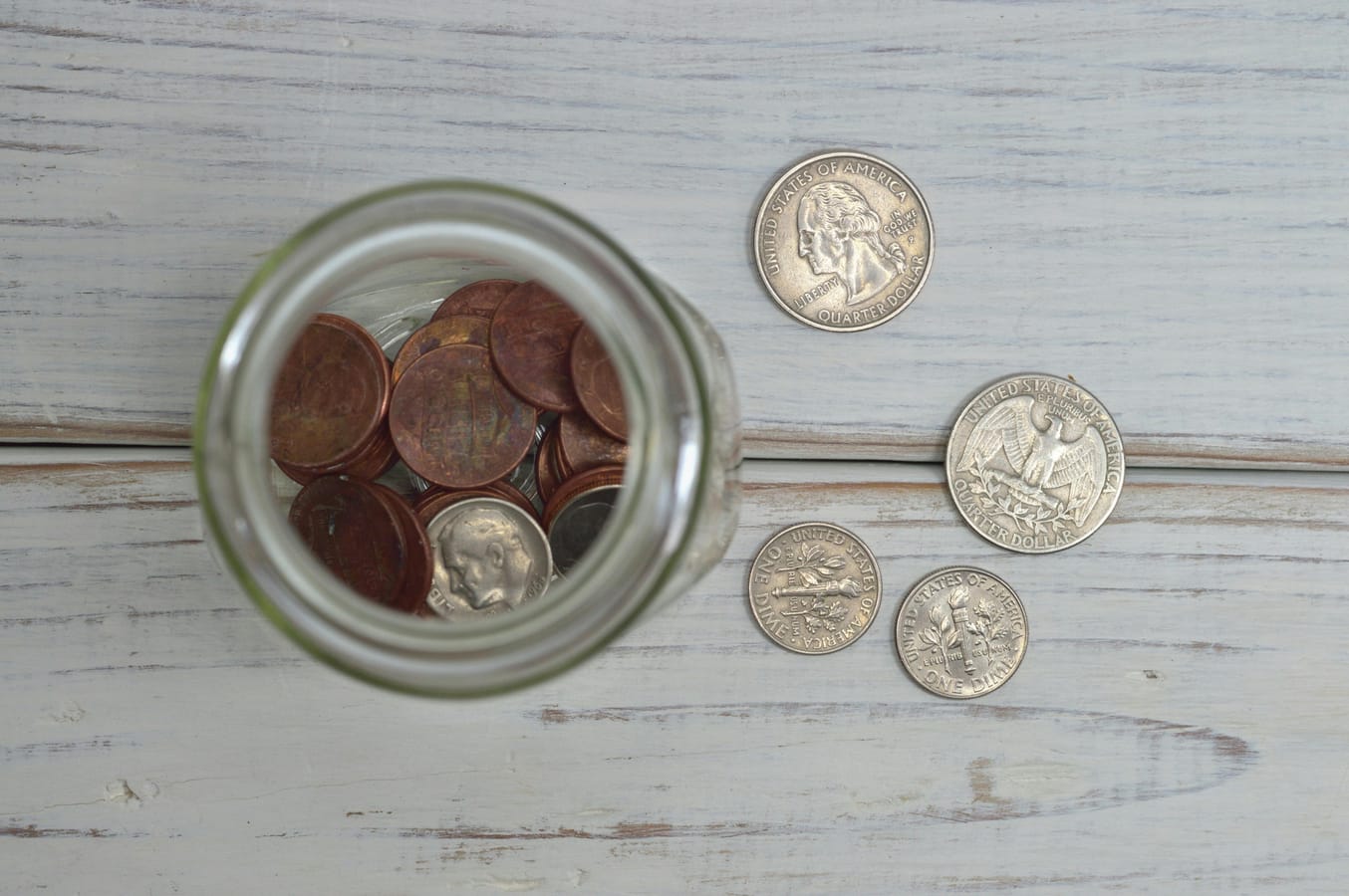 A jar of coins on a wooden table with a calendar visible in the background.