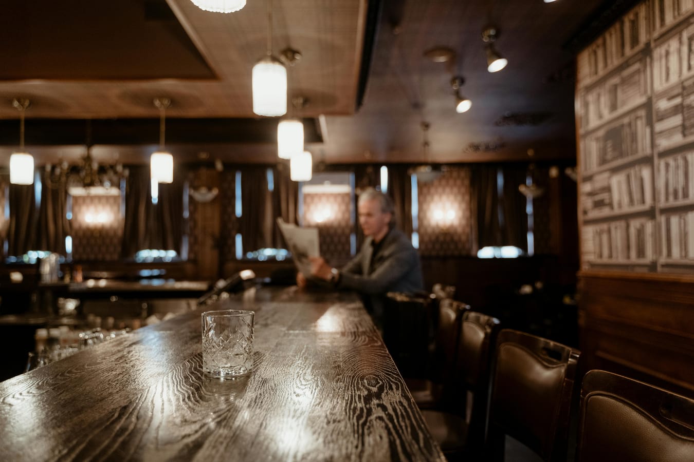 A wallet open on a wooden bar table beside an empty pint glass.