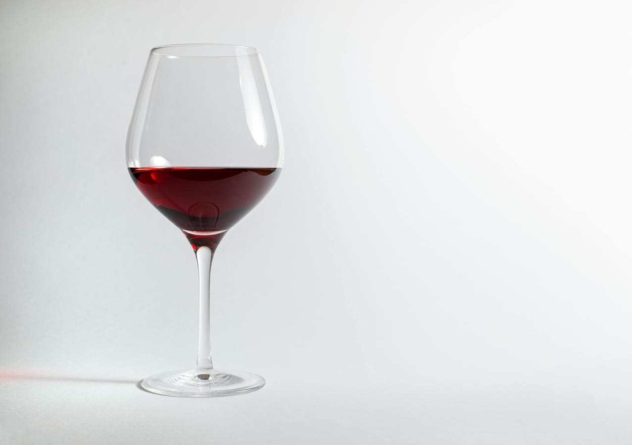 A single glass of red wine on a wooden table, half full, in soft natural light.