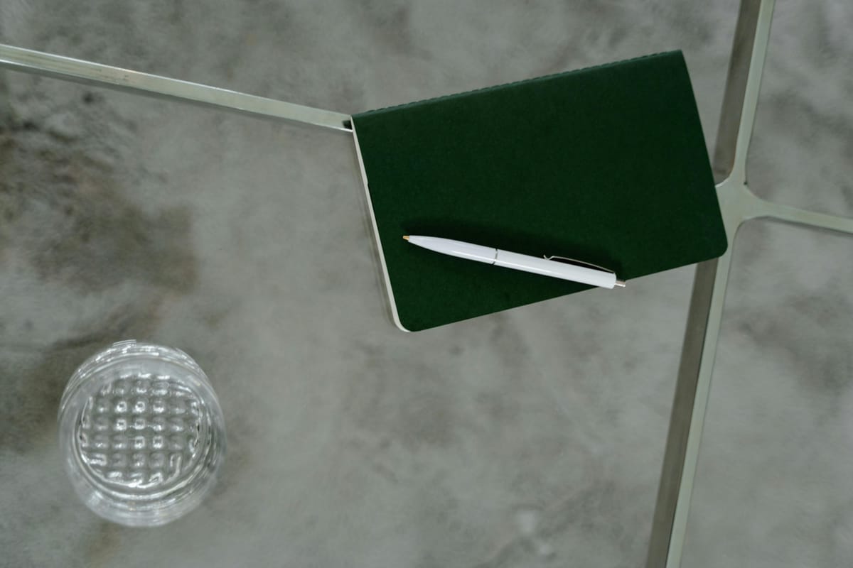 A notebook and pen on a table beside a glass.
