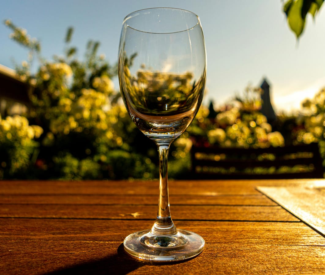 A glass of water and a glass of wine side by side on a wooden table in soft natural light.