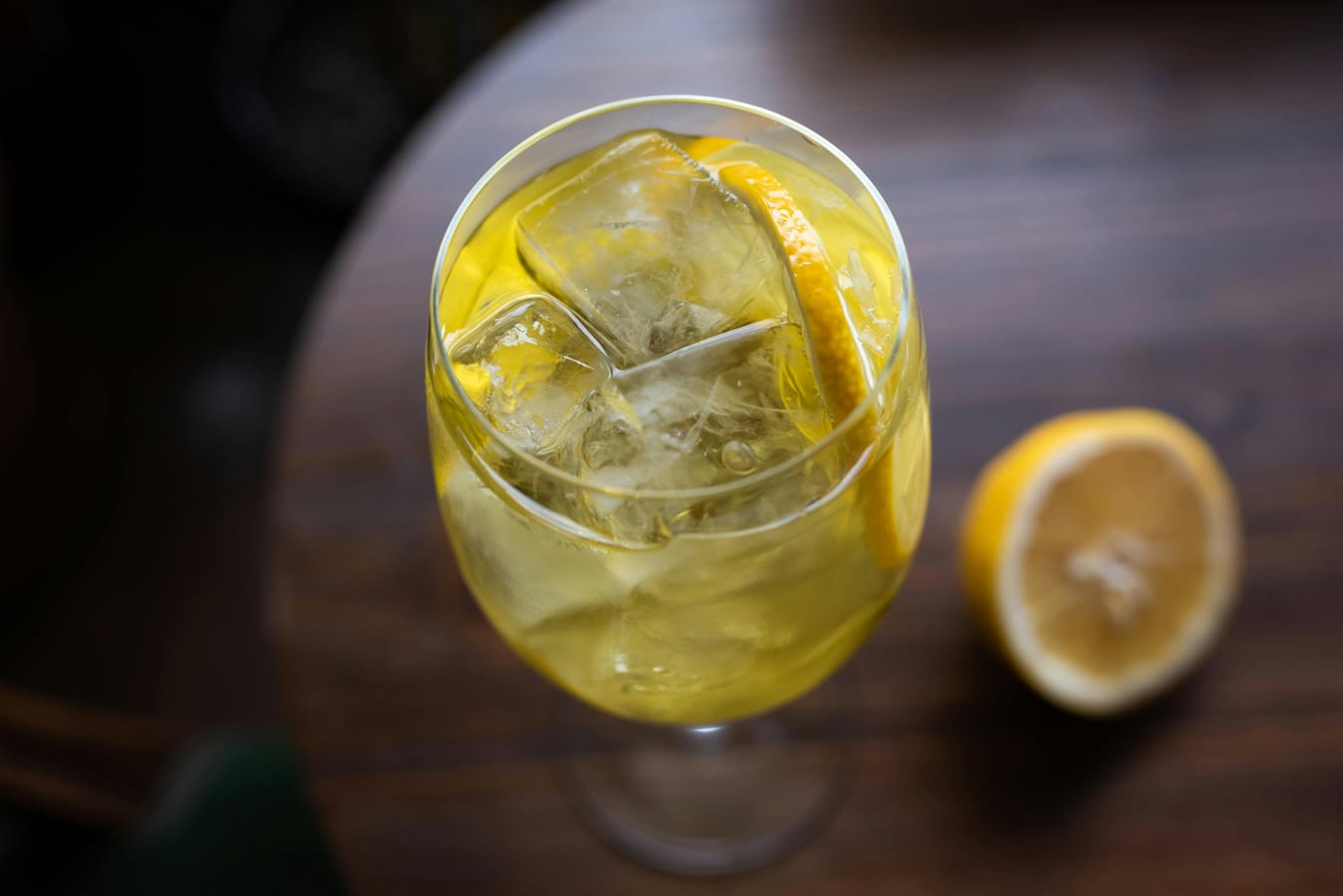 A half-full glass of wine on a wooden table beside a sparkling water with lime.