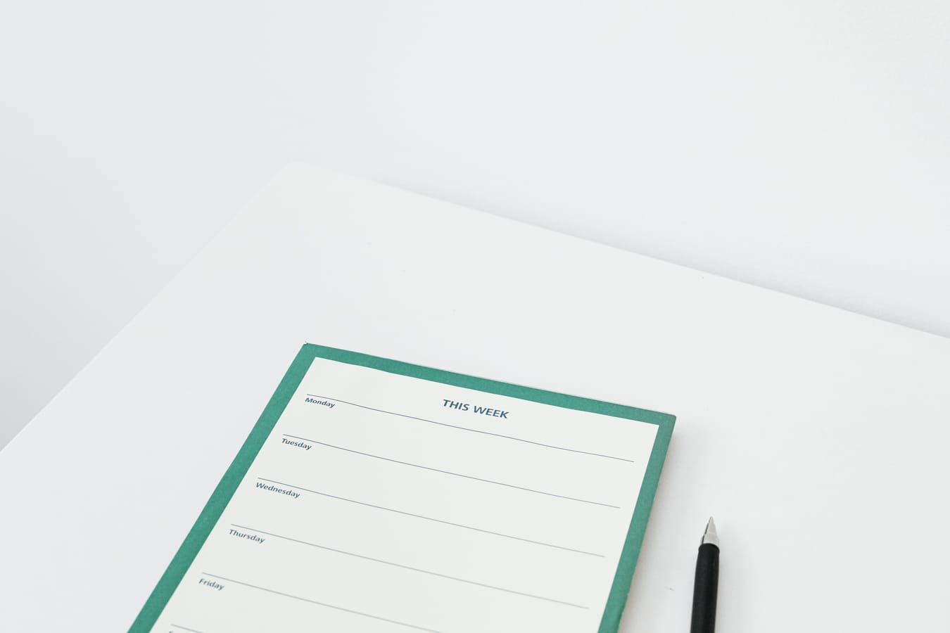 A weekly planner on a wooden desk with some days marked, beside a pen and a glass of water.