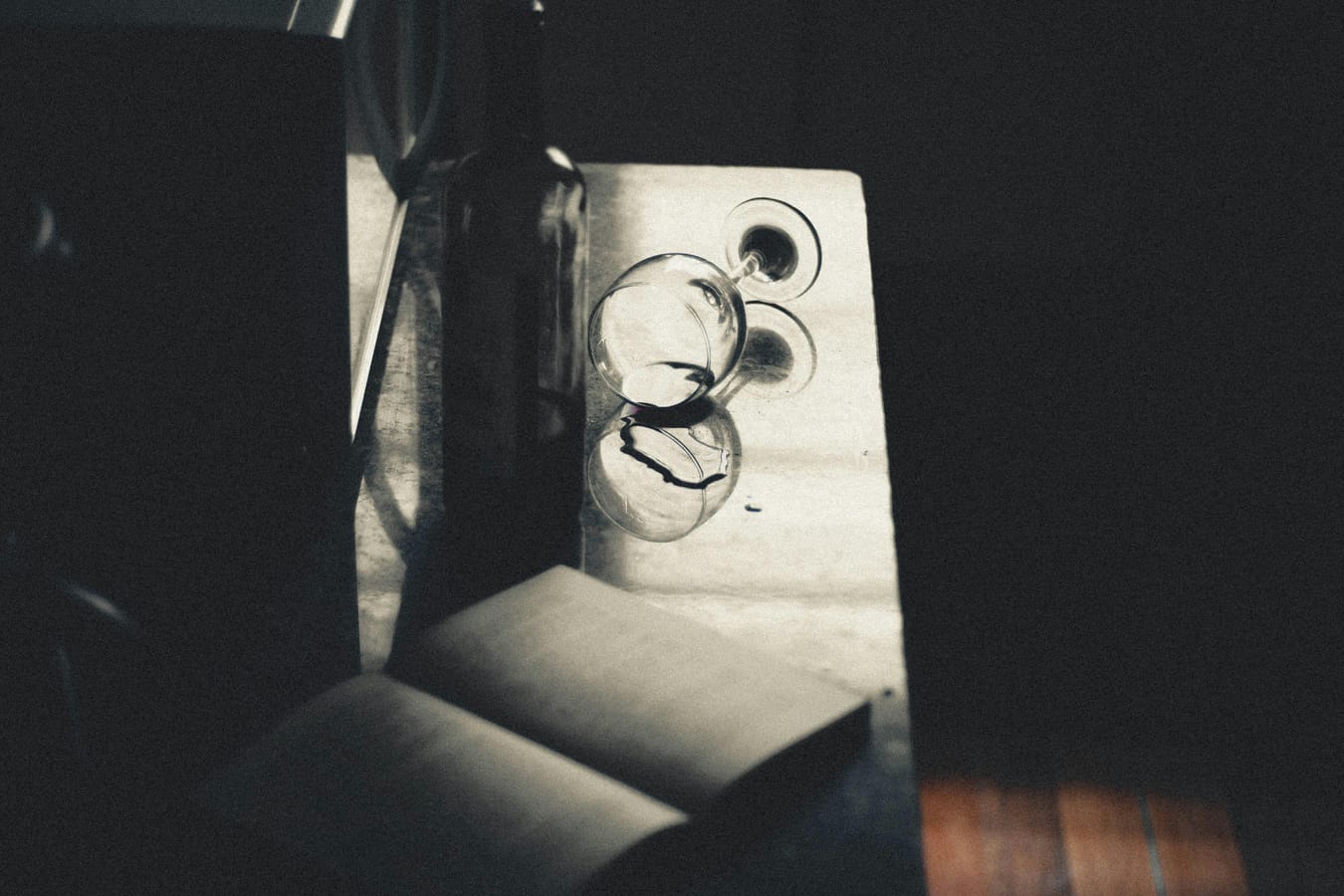 A glass of red wine on a wooden table beside an open book in soft natural light.