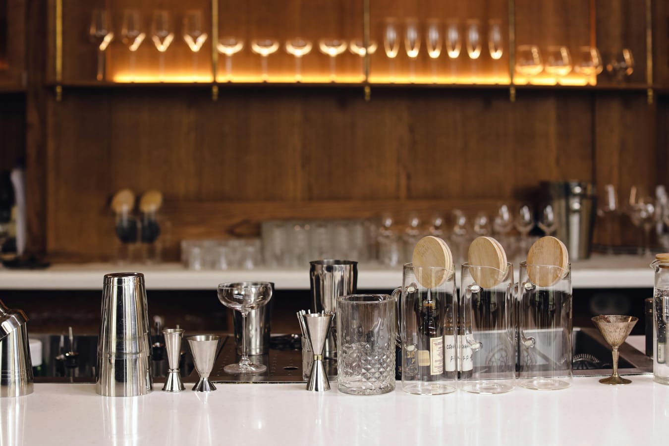 An assortment of bottles and glasses arranged on a wooden bar showing different drink categories.