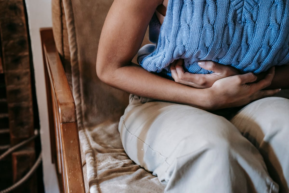 A person seated at a table resting a hand near their stomach.