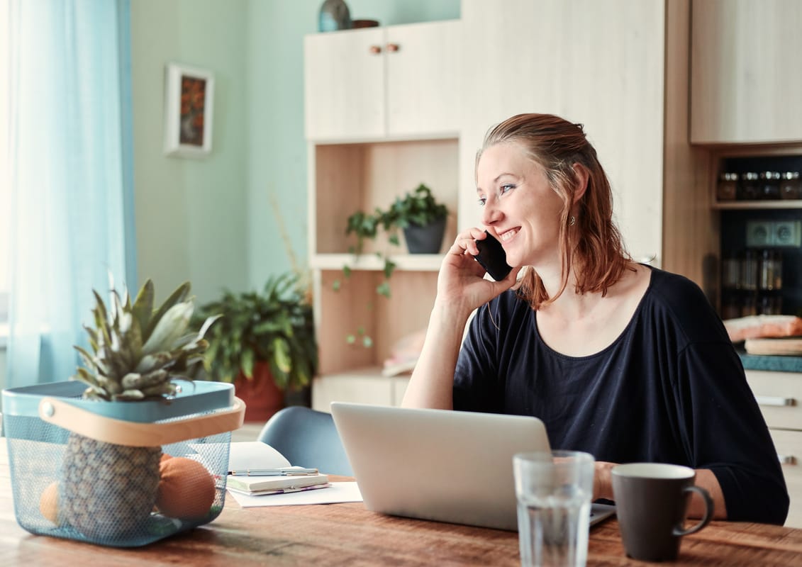 A person at a kitchen table looking at a phone beside a glass of water.