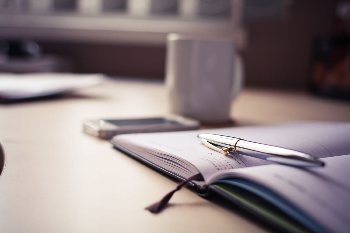 An open diary on a desk beside a pen in natural light.