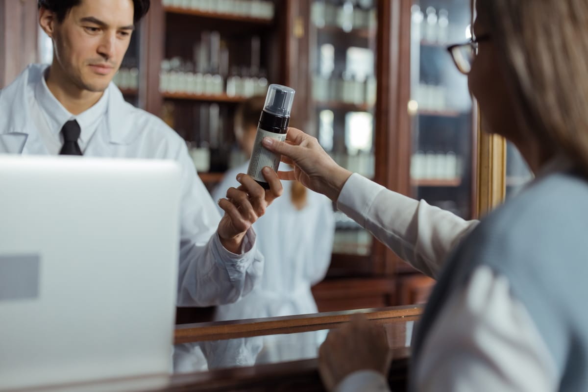 A pharmacist handing a prescription package across a counter.