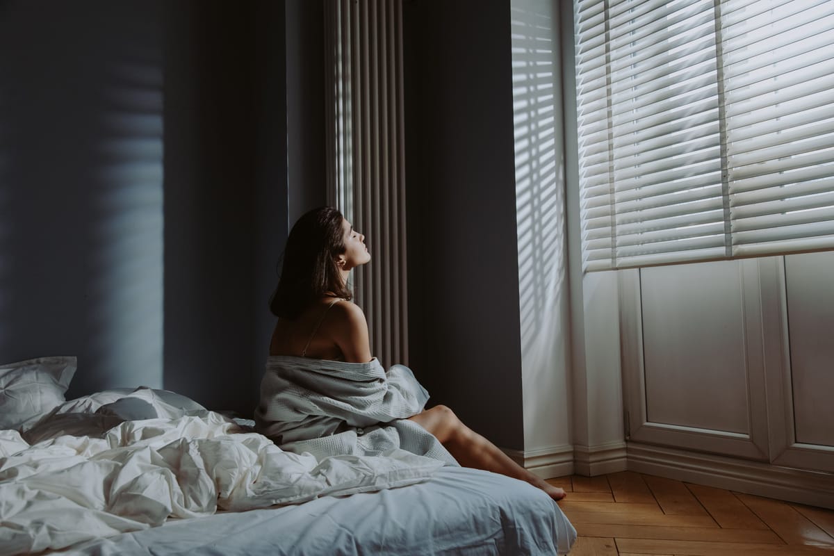 A person sitting on the edge of a bed in morning light.