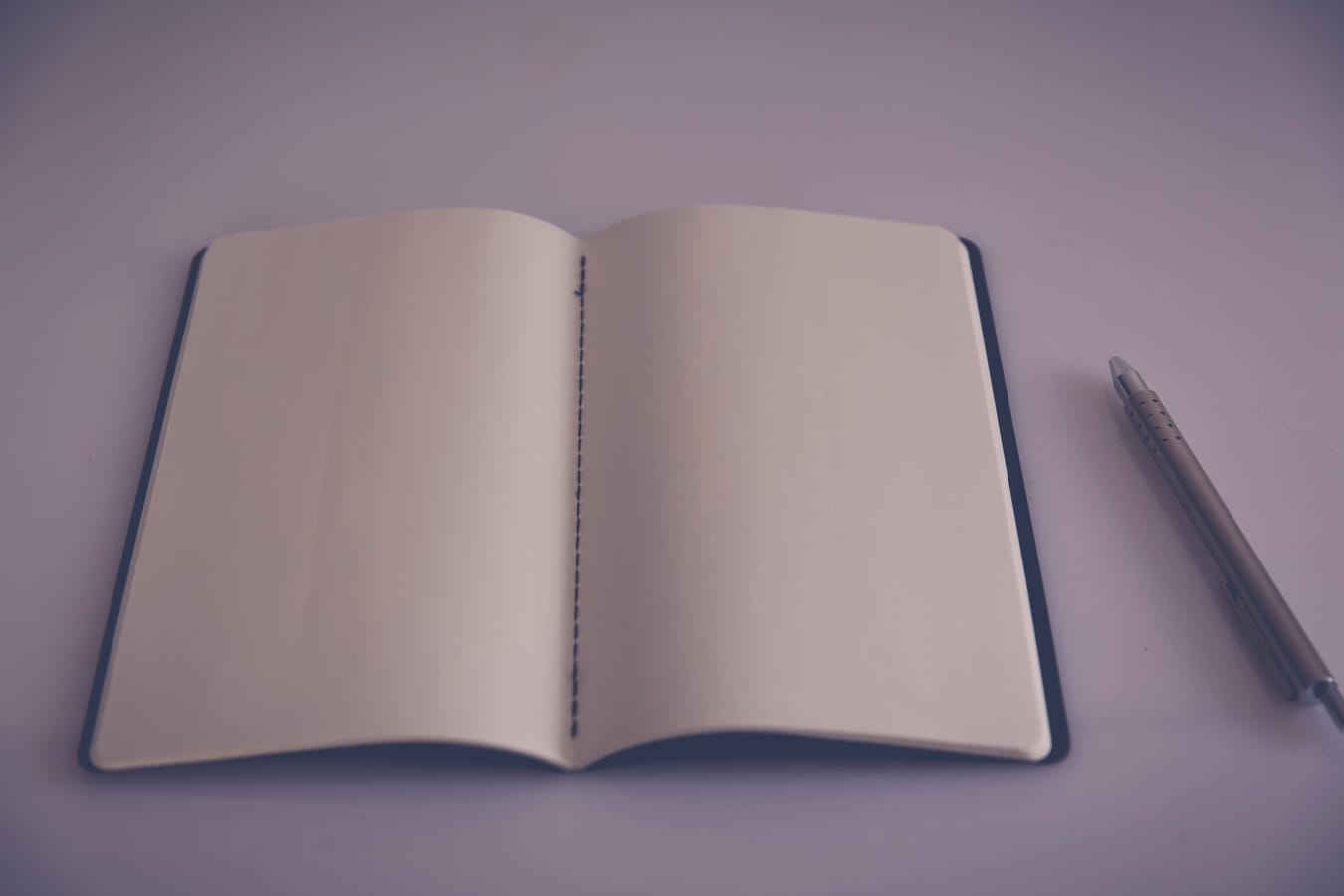 An empty notebook page and a pen on a plain desk.