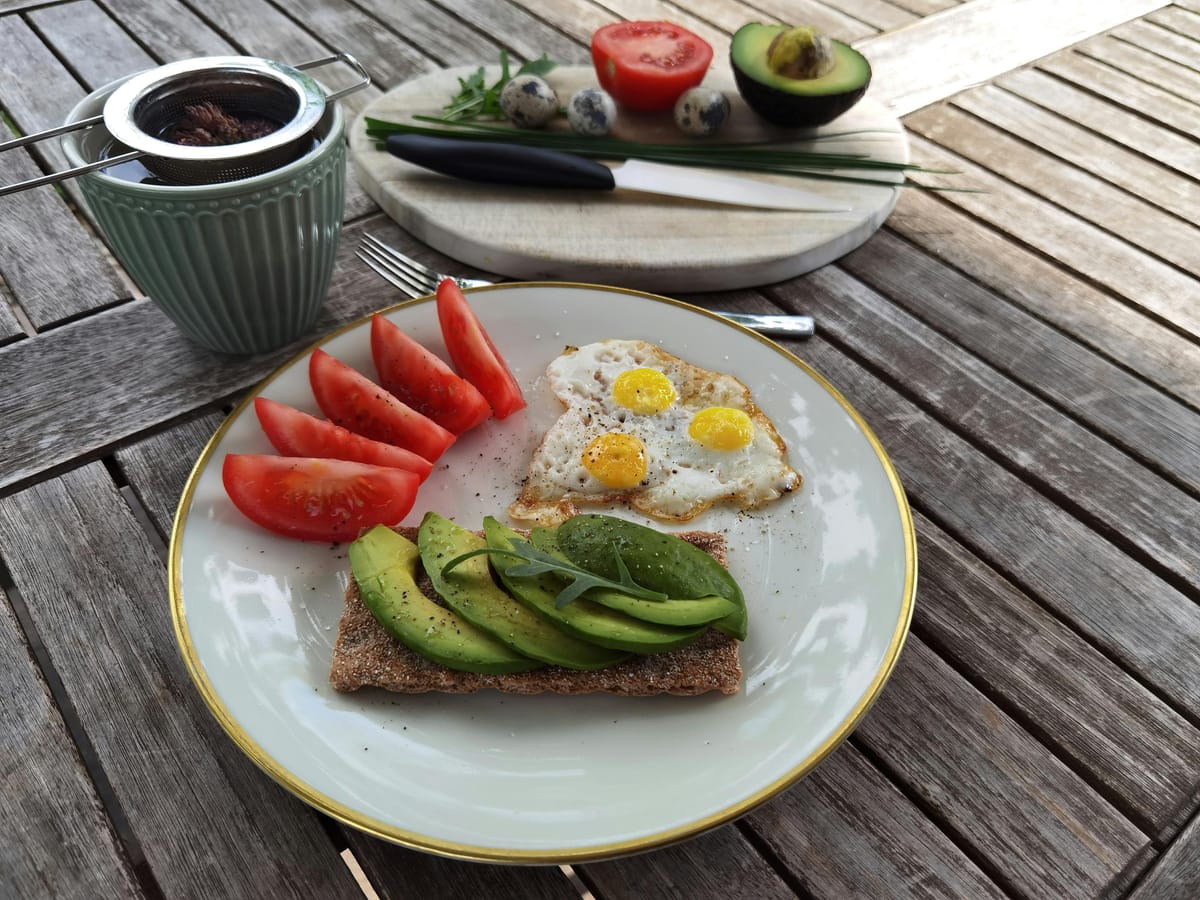 A simple meal of toast, eggs, and avocado on a wooden table in soft natural light.