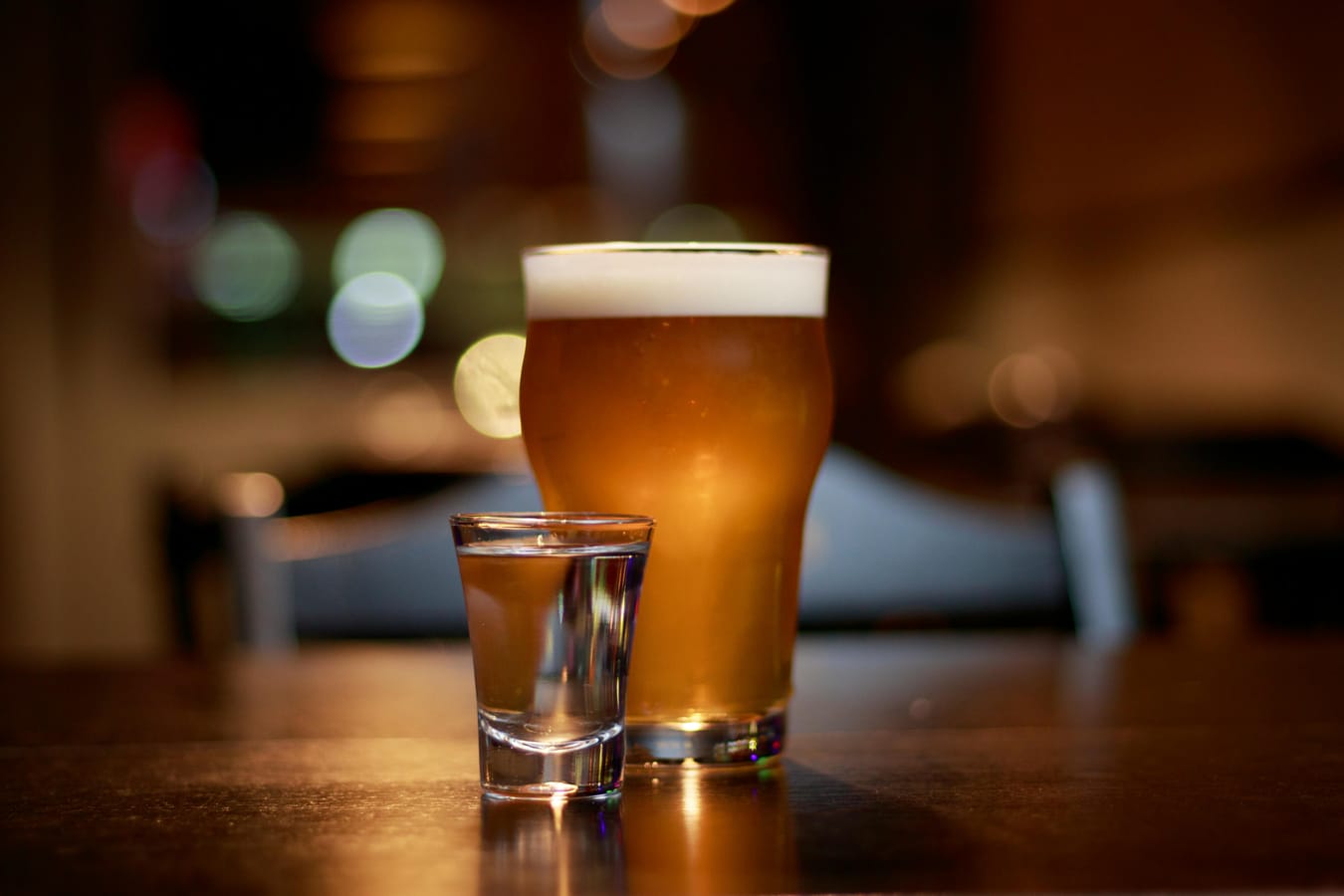 A glass of water and a half-finished pint of beer side by side on a wooden bar.