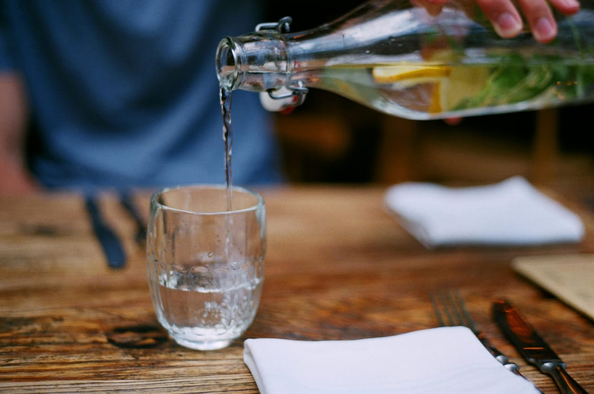 A glass being filled with water on a wooden table.