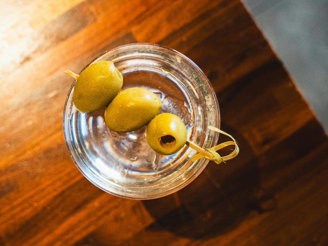 A bowl of peanuts or olives beside a glass of water on a wooden bar.