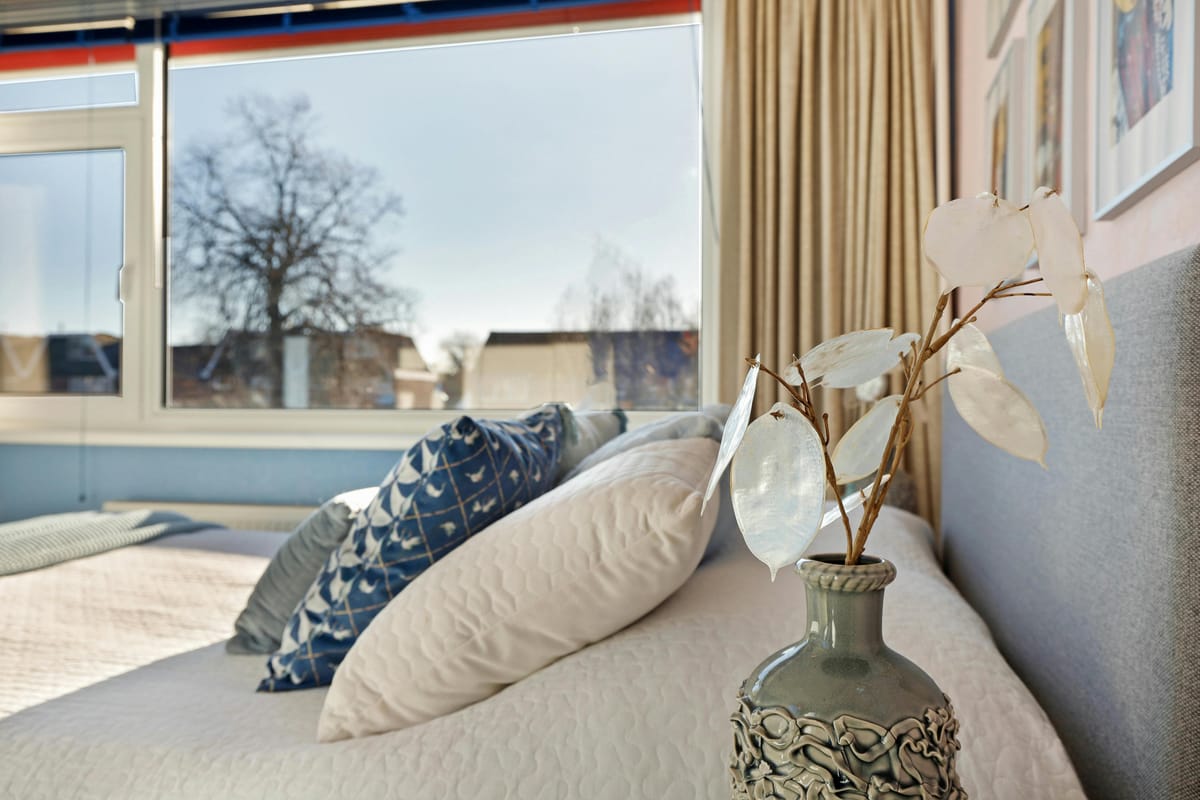 A glass of water on a bedside table with morning light through a window.