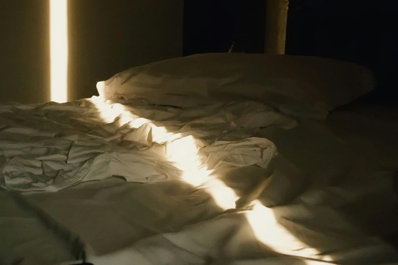 An unmade bed in a sunlit bedroom with a glass of water on the bedside table, suggesting a difficult morning.