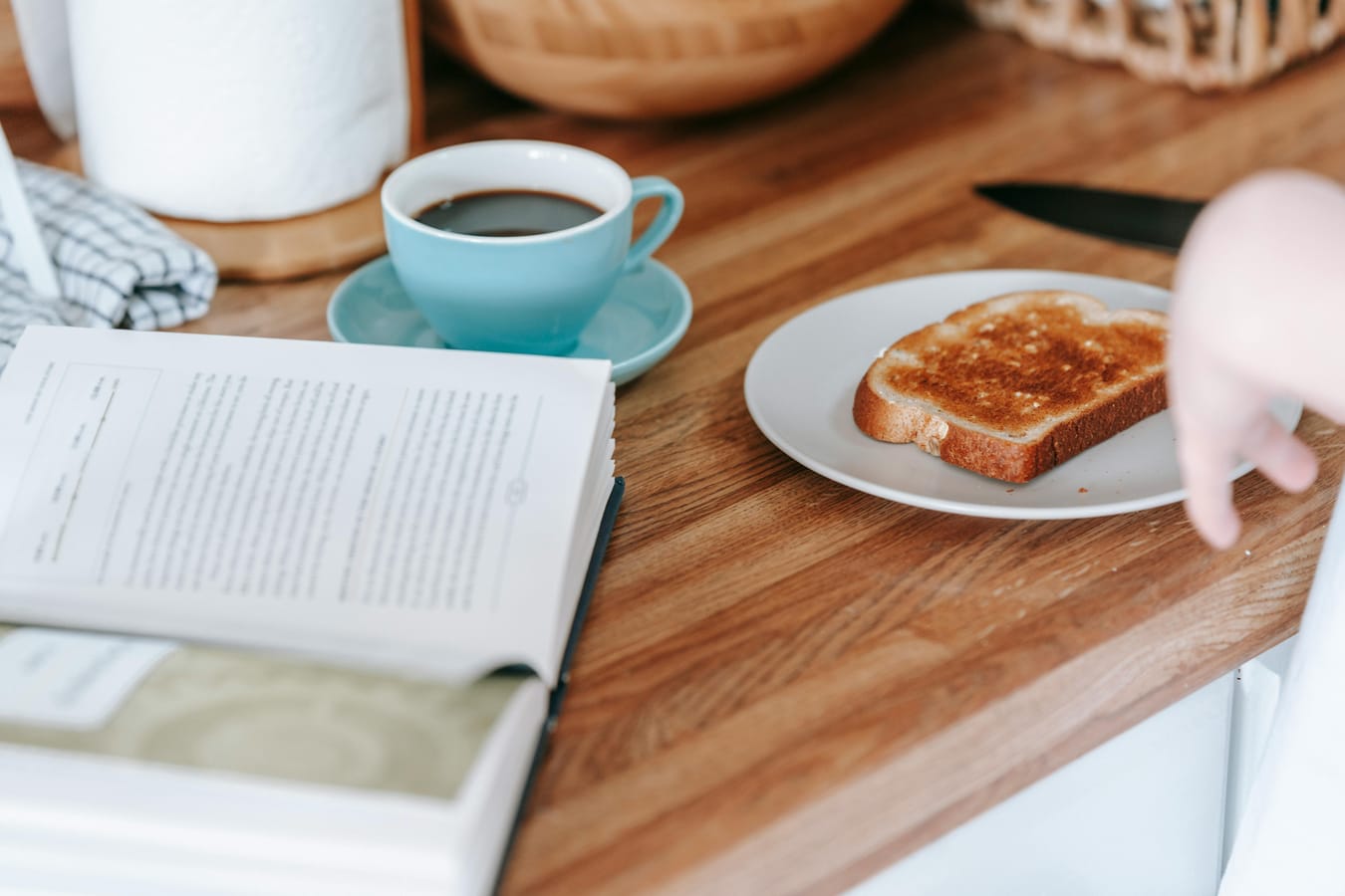 A glass of water and a piece of toast on a wooden kitchen counter in soft morning light.