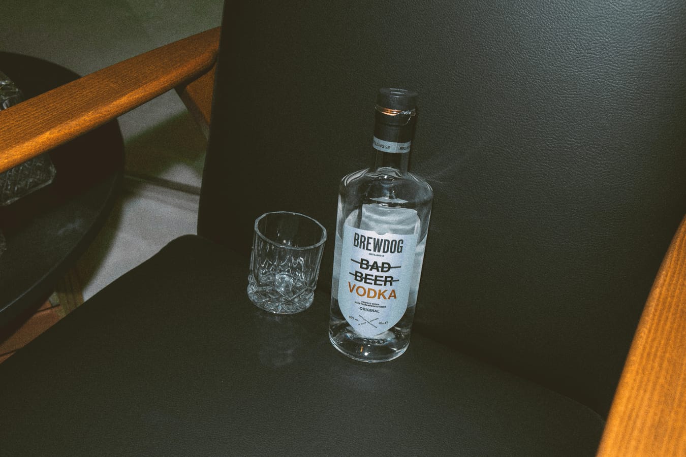 A clear bottle of vodka and a clear glass on a wooden bar in soft light.