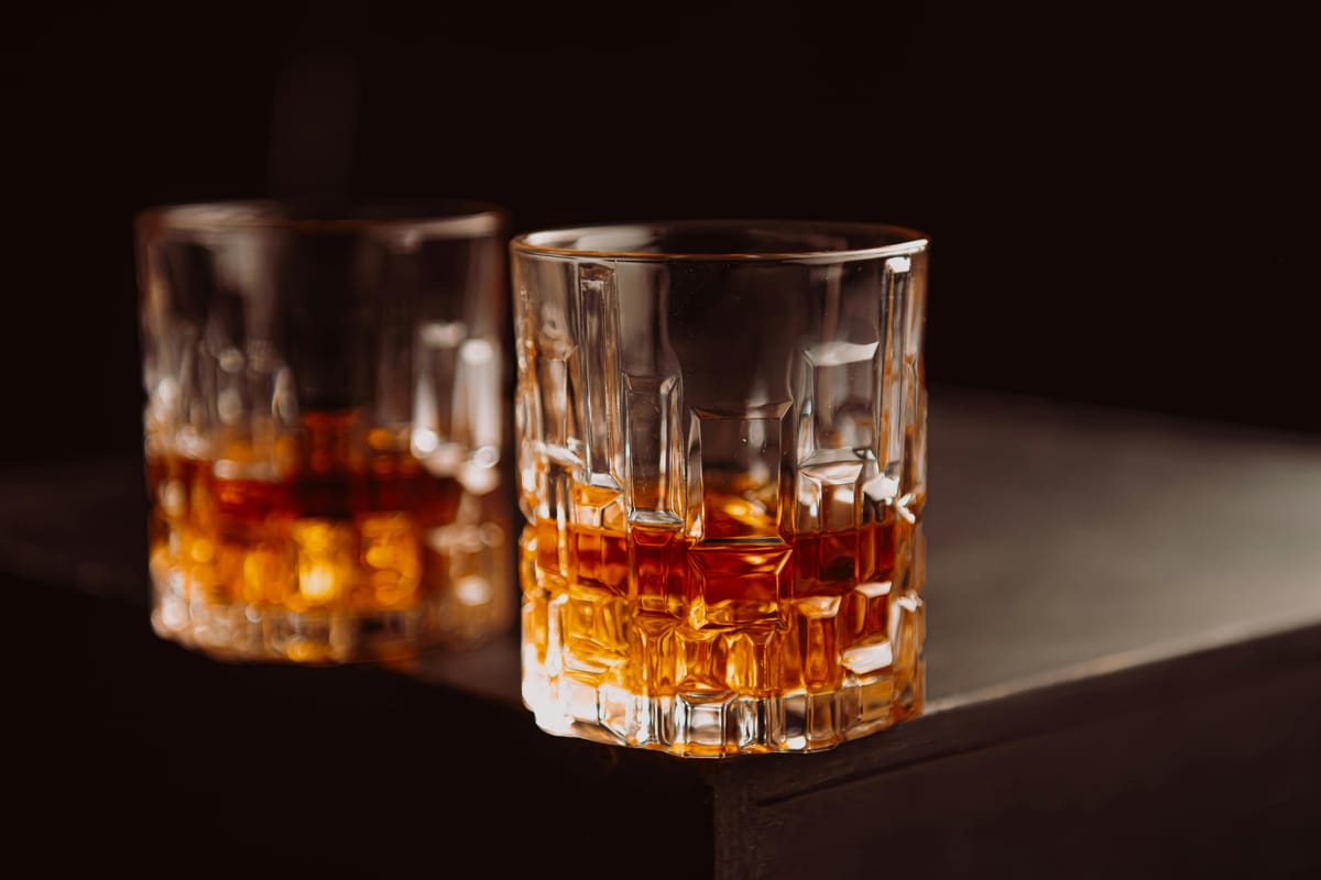 A whisky glass with amber liquid on a dark wooden table.