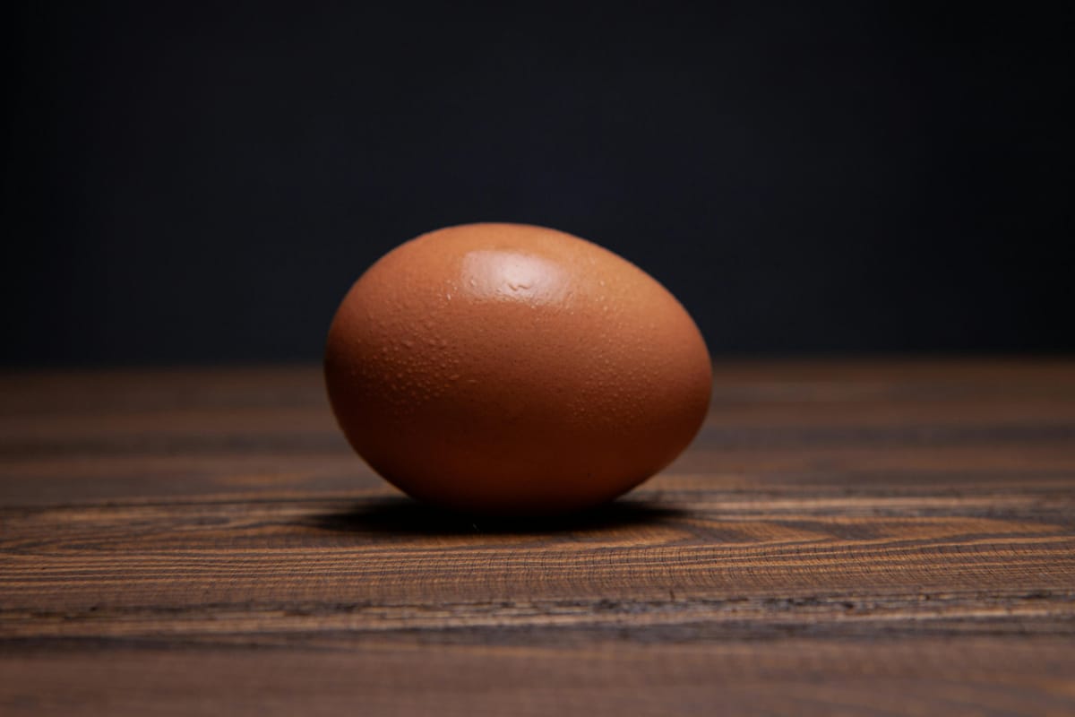 A whole raw egg in its shell on a wooden surface.