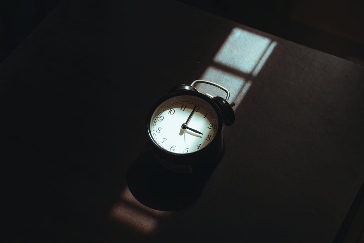 A clock on a bedside table in dim light.