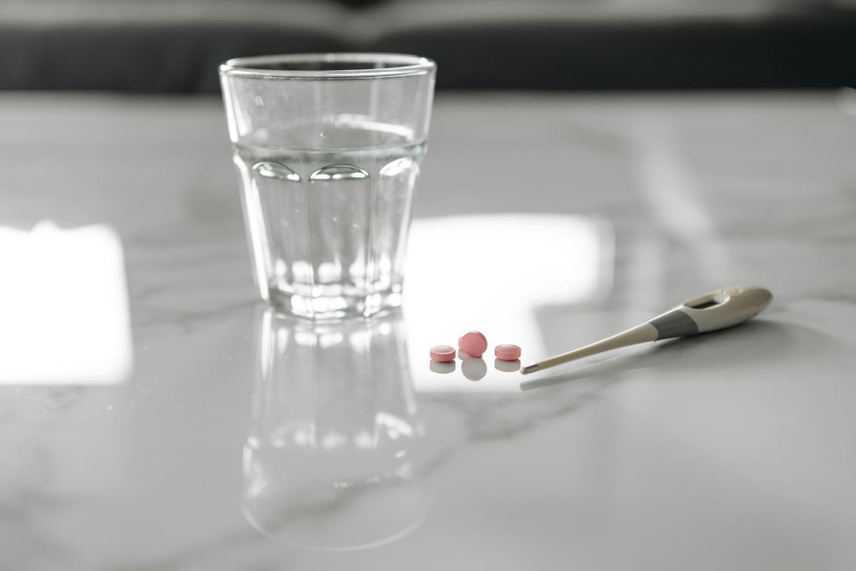 A glass of water and a small pill bottle on a wooden table.