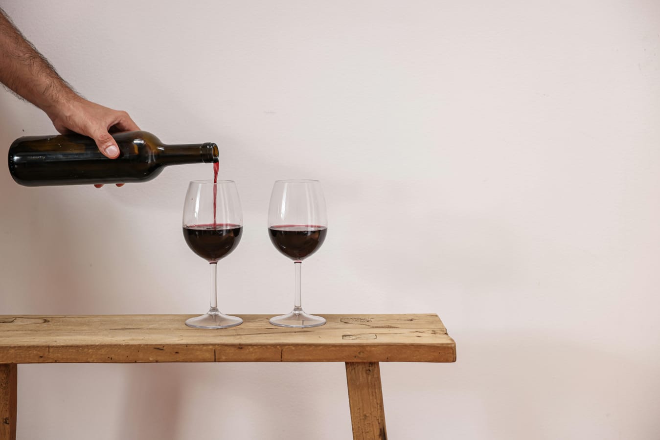 A glass of red wine and a clear glass of vodka side by side on a wooden table.