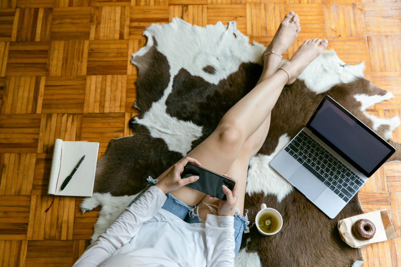 A person seated cross-legged on a wooden floor by a window with soft morning light, with a notebook and tea nearby.