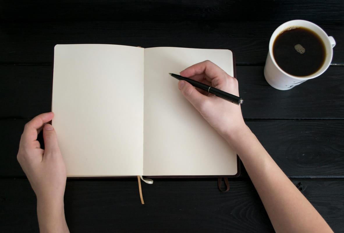 An open notebook and pen on a wooden desk in morning light.