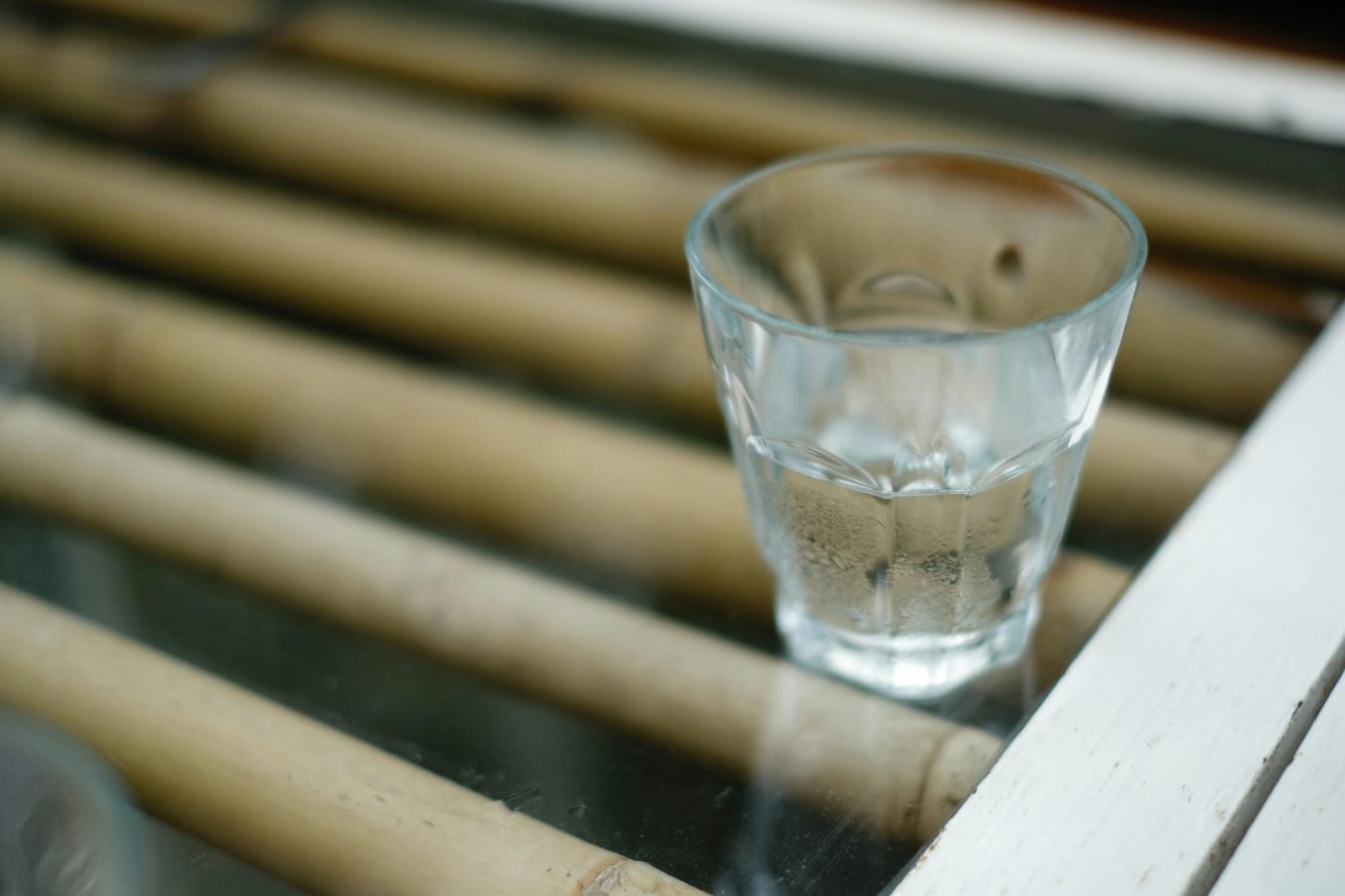 A small medication tablet on a wooden surface beside a glass of water in soft natural light.